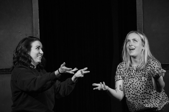 Hannah and Lizzie, arms out while improvising, on stage as the Shrieking Harpies