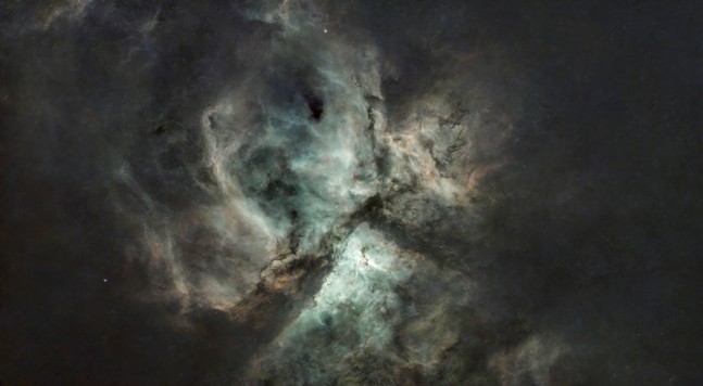 A starless nebula, roughly divided in three by an inverted 'Y' of dust lanes. The centre is a blue green, fading to a pinky-orange around the edges.