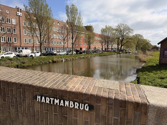 A smaller Amsterdam canal viewed from a brick bridge overpass.