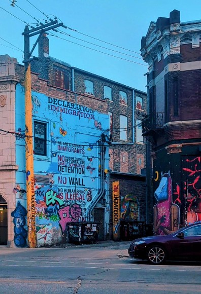 Mural on the side of a Chicago walkup with a baby blue background. Reads "Declaration of Immigration" and phrases such as "no wall", "no human being is illegal" and "no deportations"