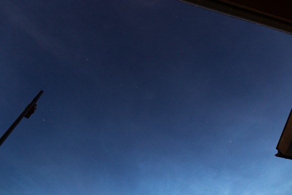 A blue twilight sky with some high altitude clouds, already filled with some stars. The silhouette of a LED streetlight is visible at the left, but the light is off, allowing a clear view of the sky, without light pollution.