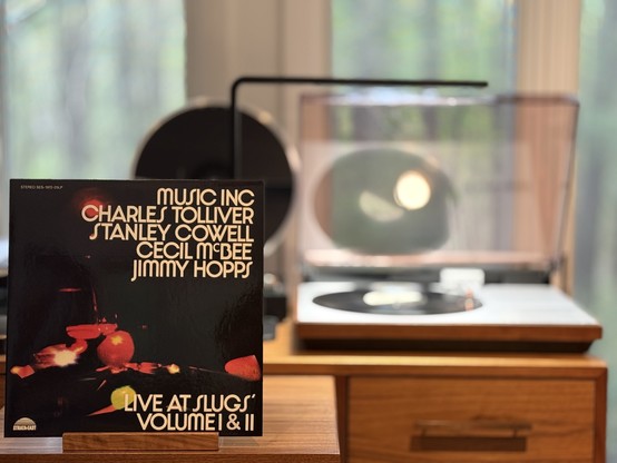 Music Inc. - Live at Slugs - Volume I & II LP cover.

Black cover with what look to be blurred out lights.

The black LP plays on a vintage, restored Bang & Olufsen Beogram 4000 linear-tracking turntable to the right.