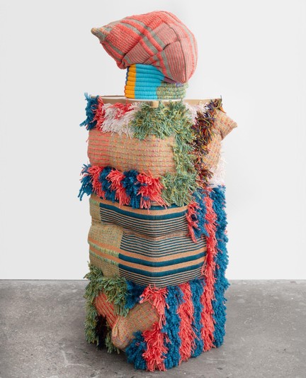 a colorful, abstract textile sculpture with different textures, primarily a tall rectangle with a sac-like shape on top
