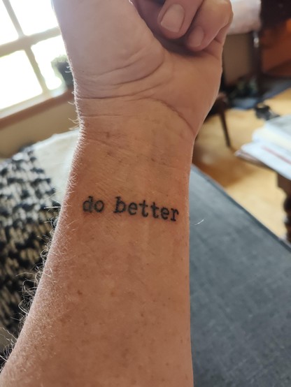 A wrist is presented, left hand partially visible, on the wrist in dark gray ink are the words "do better".