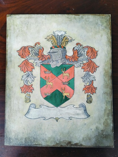 a family crest design, it is a silver helmet facing left, floral designs aching out from both sides, a shield under the helmet, it has 3 crowns and 3 stags on it on a ed x on a green field, underneath is the banner where the last name will e added at the end