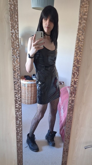 Non binary person in a black shiny dress and fishnet tights