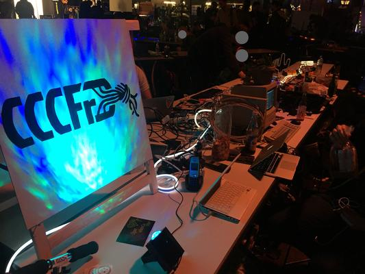 CCCFr Banner auf einem Congress der letzten Jahre - beleuchtet mit einem Wassereffekt und Lichterkette auf dem Tisch voller Technik wild verteilt