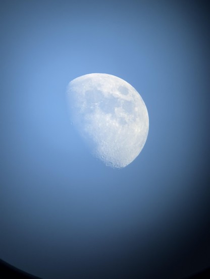 Unedited original version of the previous image, with the moon washed out by sunlight and the black edges of the telescope eyepiece visible at the corners.