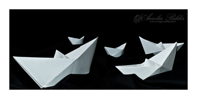 Papierschiffchen aus weißem Papier auf einem schwarzen Tuch.