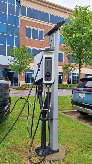 Blink-brand EV charging station for electric vehicles outside an office building. Grass, pavement, 2 vehicles.