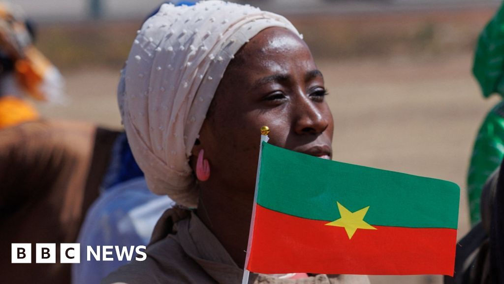 A woman wearing headscarf and pink earrings waves the flag of Burkina Faso