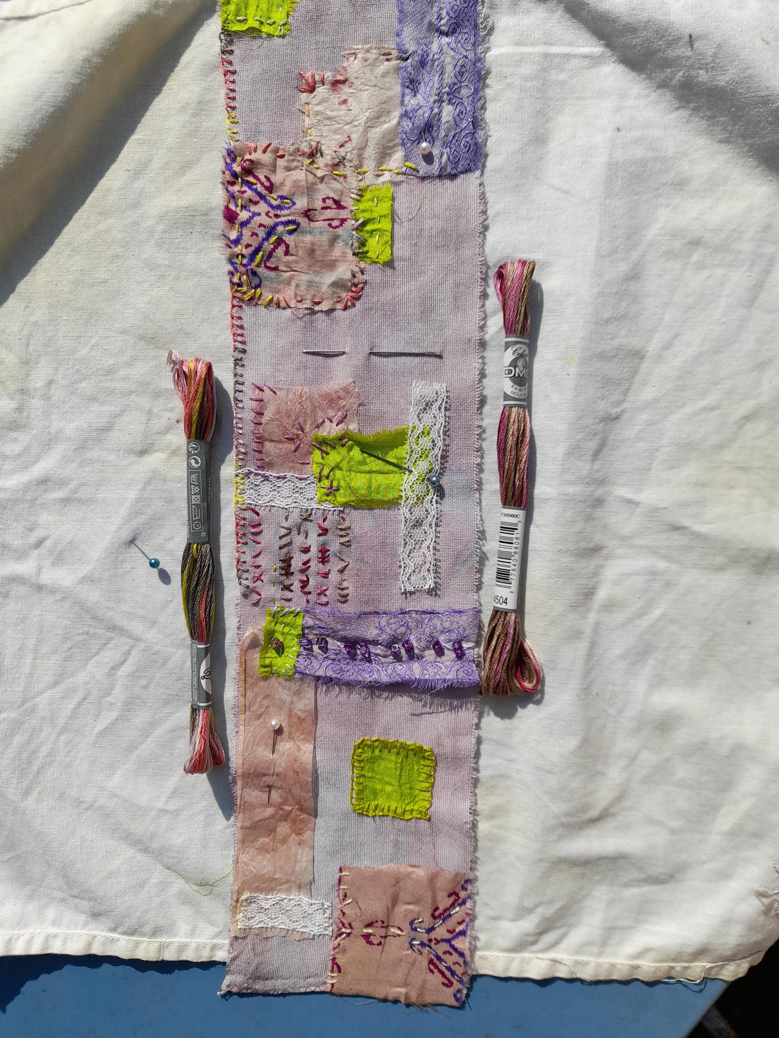 A wide band of cotton flannel that is later wrapped around an old bobbin. The fabric is light purple, dyed with red fruit tea. Pieces in the colour spectrum of pink, purple and yellow-green are applied like a collage: saree silk, lace, used tea bags, glass beads. They are attached with intuitive stitches, wild embroidery.