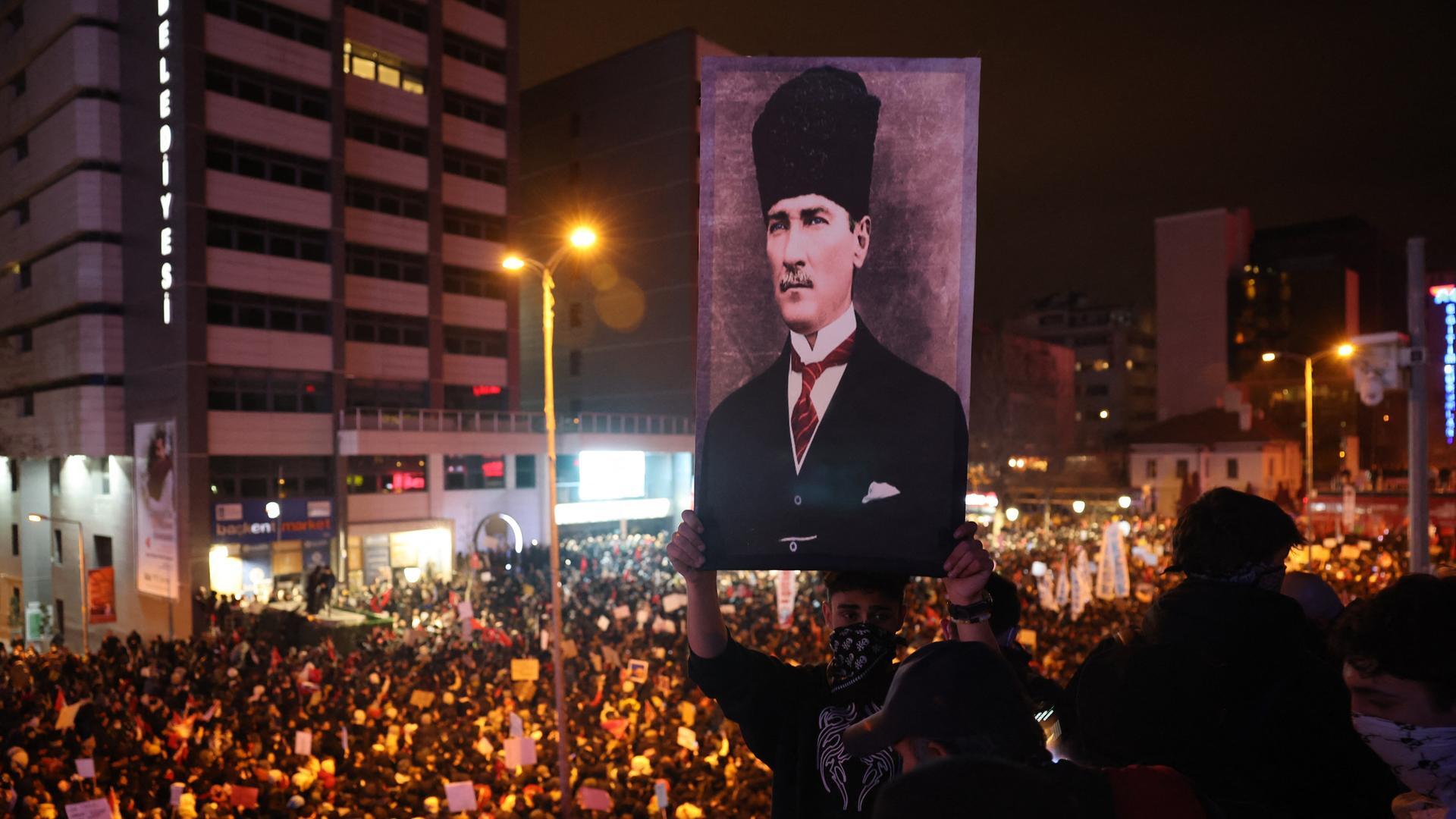 Ein Mensch hält ein Bild Mustafa Kemal Atatürks in die Höhe. Hinter ihm sieht man zahlreiche Demonstranten.