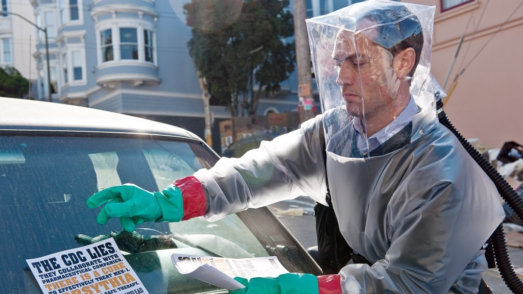 Jude Law wears a makeshift hazmat suit and puts a "the CDC lies" flier in a windshield in a still from 'Contagion'.