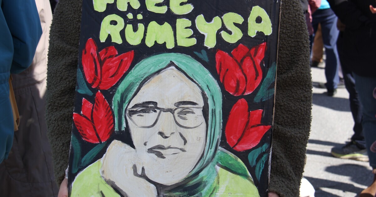 A painted sign shows a woman wearing glasses and wearing a head covering with the words "free Rümeysa" A painted sign shows a woman wearing glasses and wearing a head covering with the words "free Rümeysa"