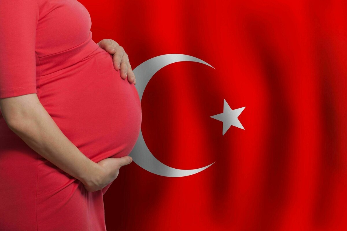 Eine schwangere Frau in rotem Kleid hält ihren Bauch vor einer türkischen Flagge