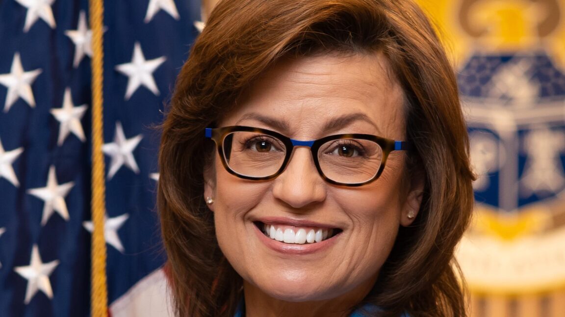 Photo of FCC Commissioner Anna Gomez standing in front of an American flag.