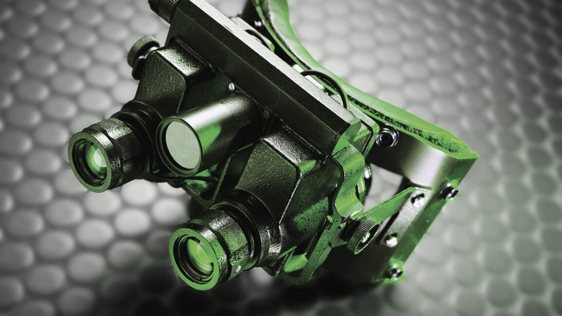 Image of bulky night vision goggles made of black material, but lit with a green light.