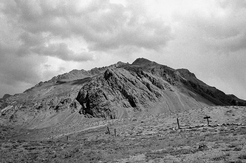 a black and white photo of a mountain in front of a dark sky with white clouds
