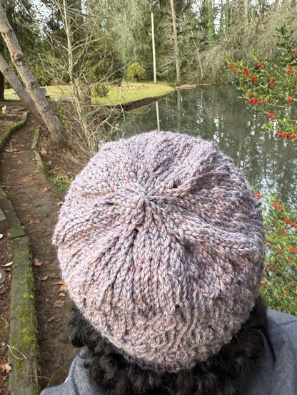The back of a hat on a head - plum colored, and among greenery.