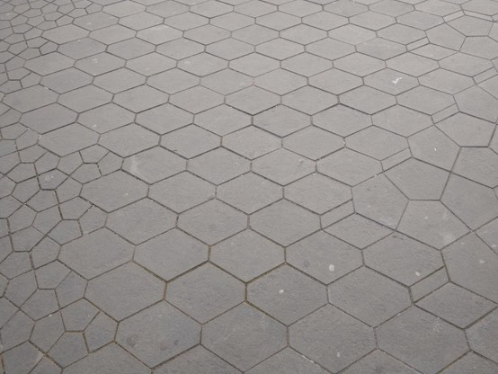Photograph of grey street paving that consists of symmetrical pentagons in in symmetrical hexagons. The middle has medium-sized hexagons; the left has pentagons inside the hexagons; the right has bigger hexagons with pentagons inside.