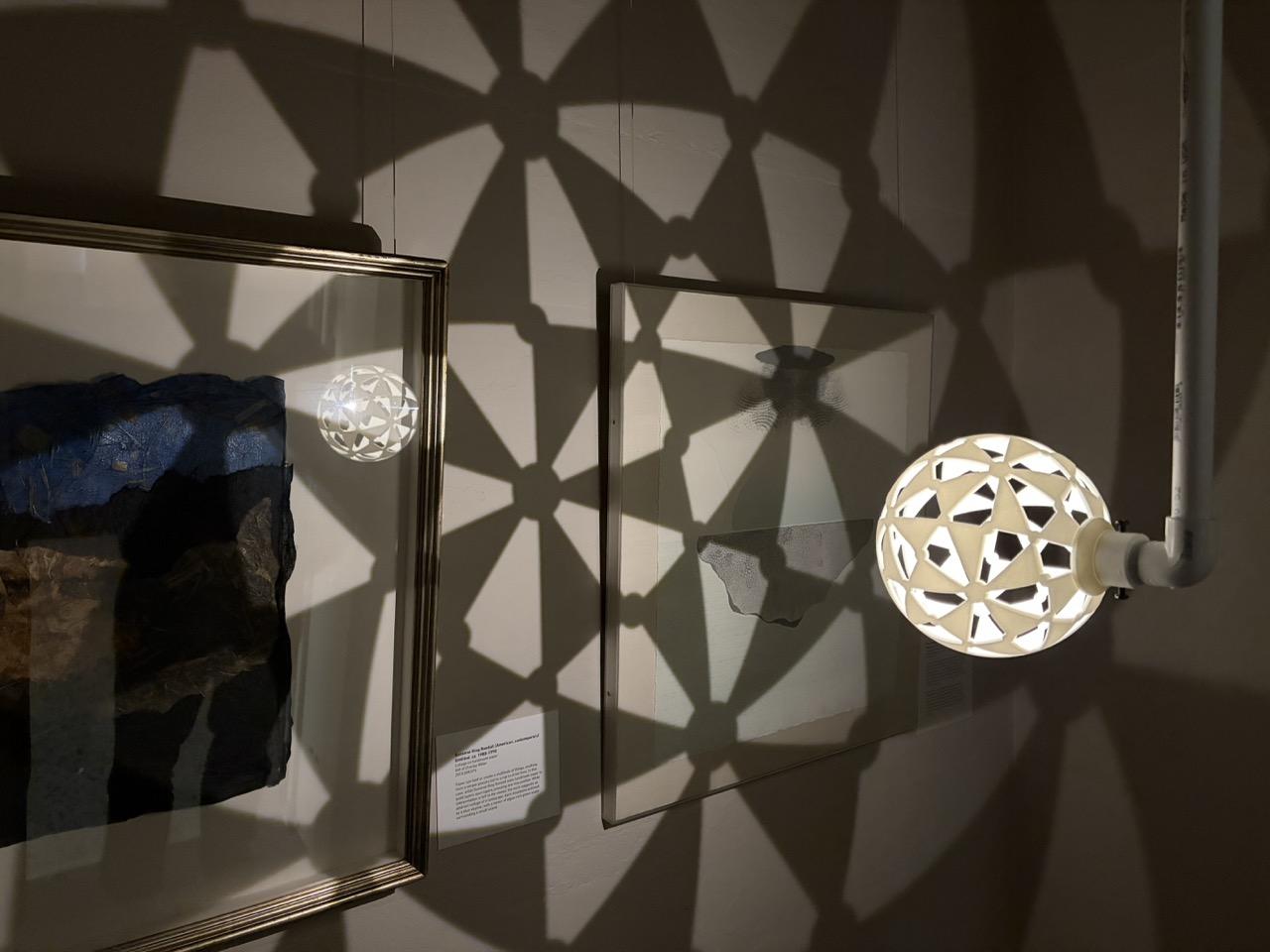 A 3D-printed sphere is patterned with triangular holes. It casts shadows onto the wall.