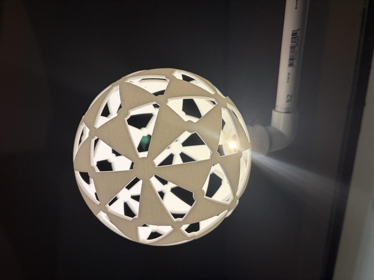 Closeup of the 3D printed sphere. It is mounted on a pipe coming down from the ceiling, which also holds an LED light.