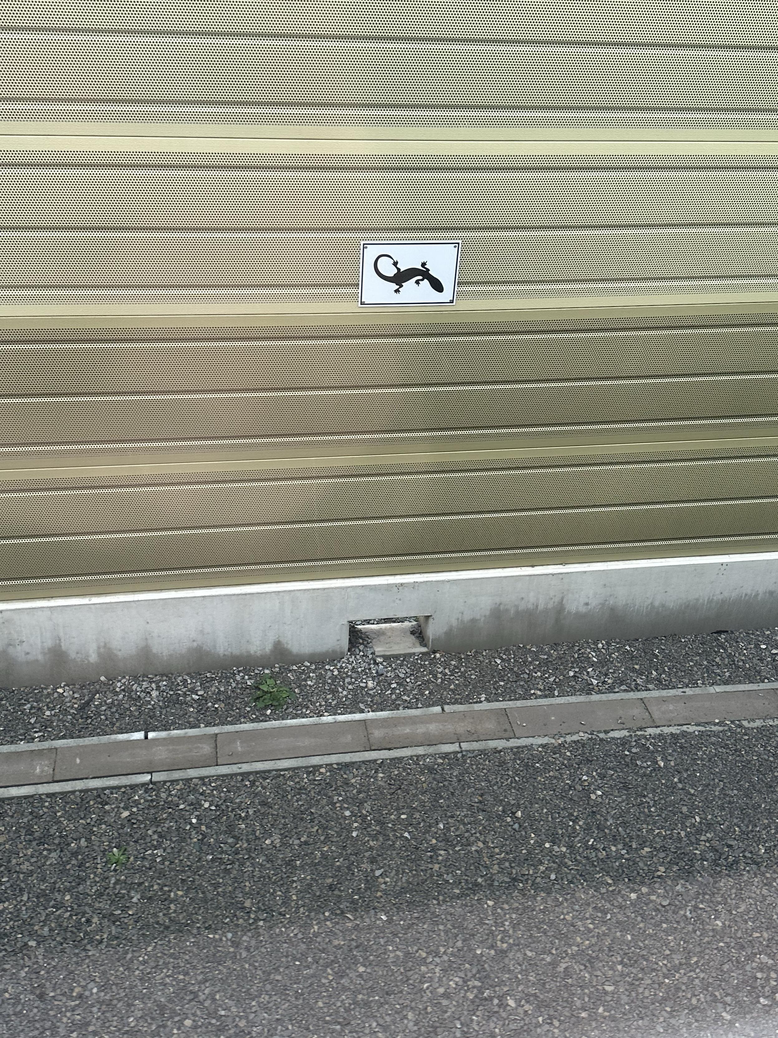 A sound wall sign a small sign showing a silhouette of a lizard, with at ground level a hole in the wall.