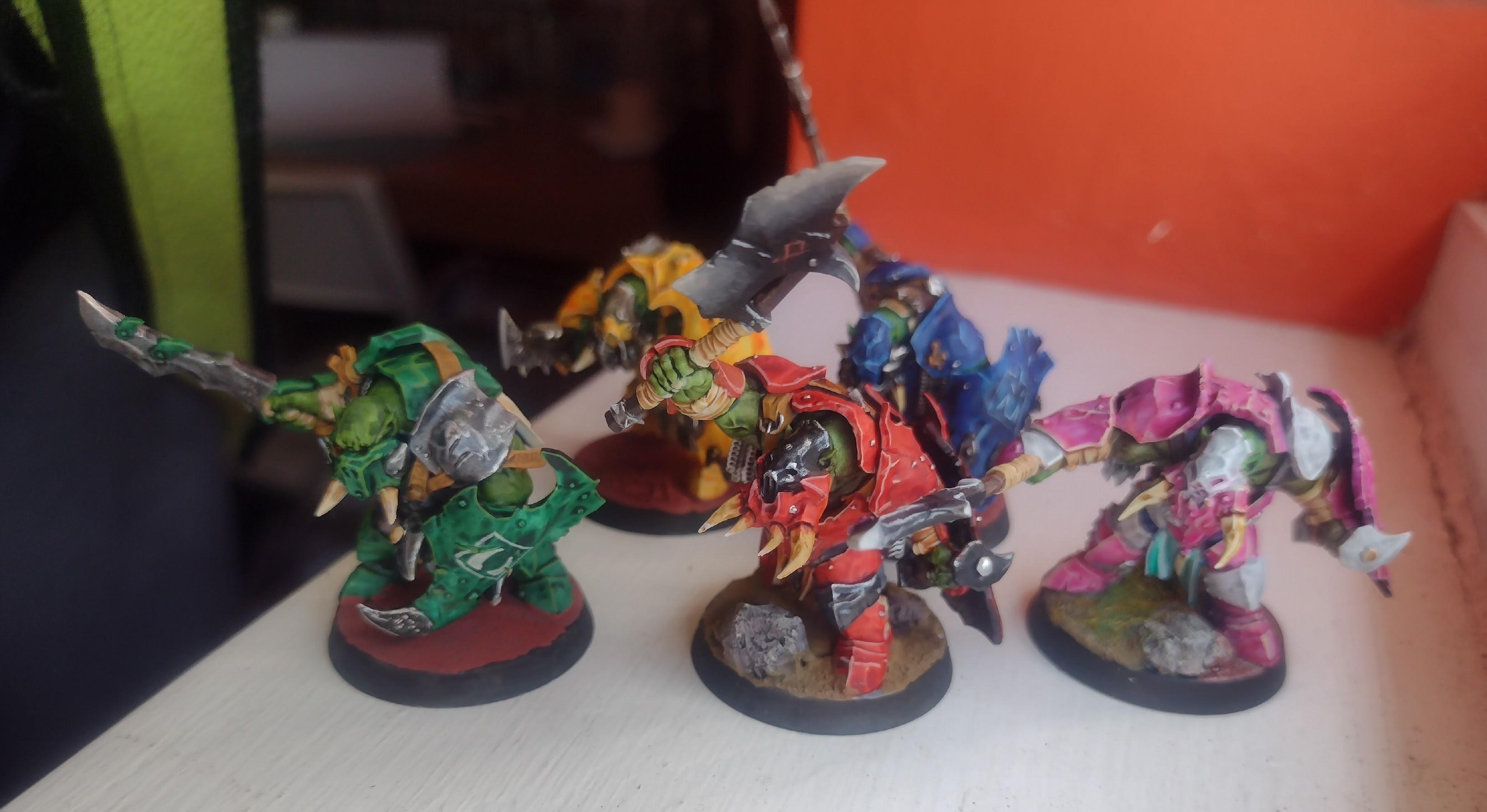 5 painted orc miniatures, one in red armour, one in blue, one in green, one in pink, and one in yellow.