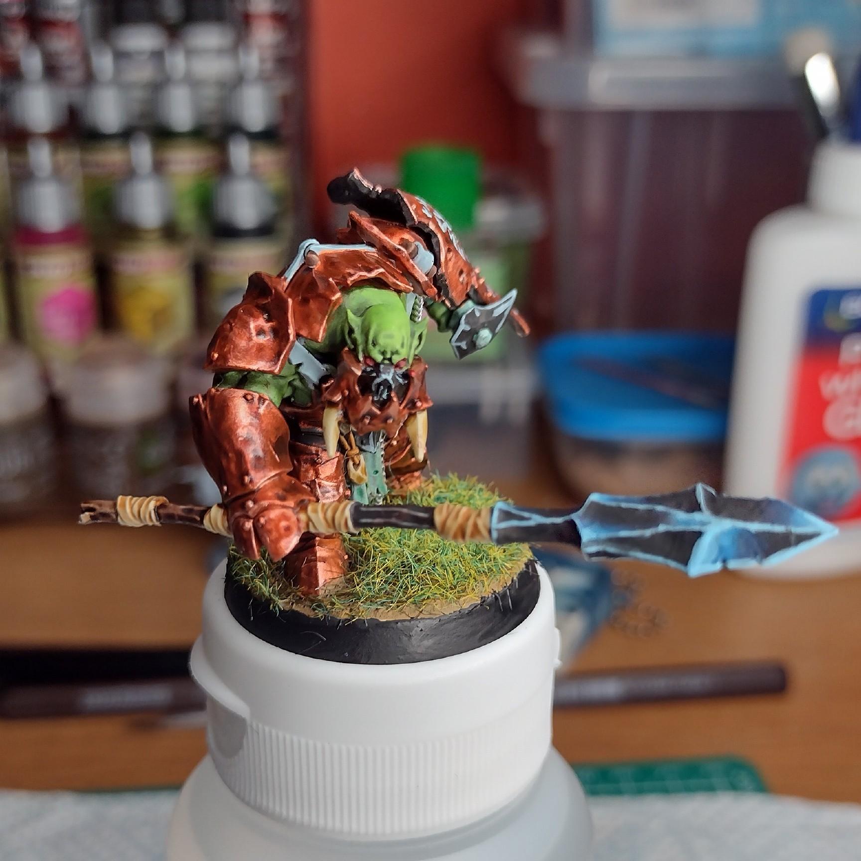 Orc miniature painted with a copper armor. In the right hans it holds a big sphere with blue reflections