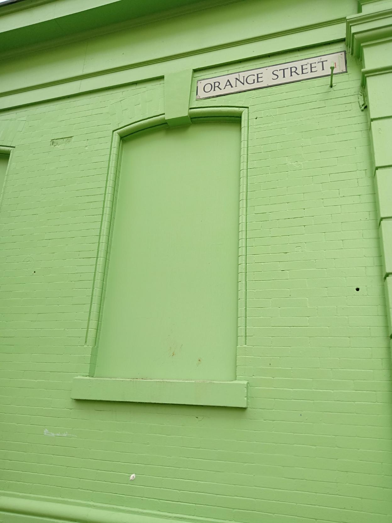 House wall and windows painted in green. Sign: Orange Street