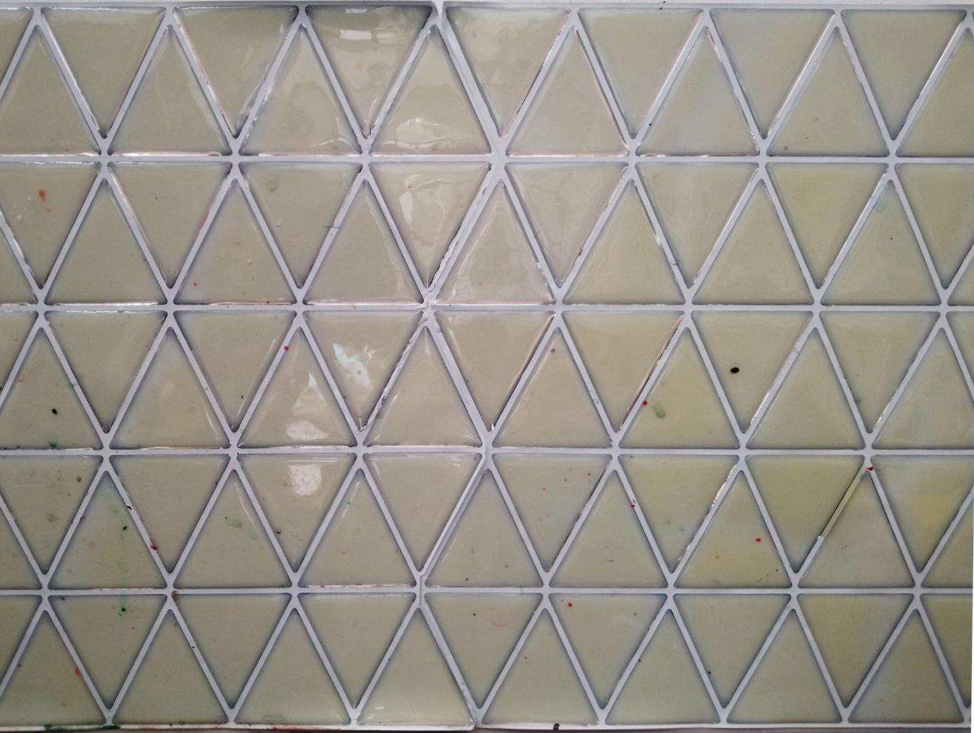 A photo of a splashback made of pale green tiles that are equilateral triangles. The grey grouting separating the tiles is wider is some places than others. The tiles are shiny but are not pristine.
