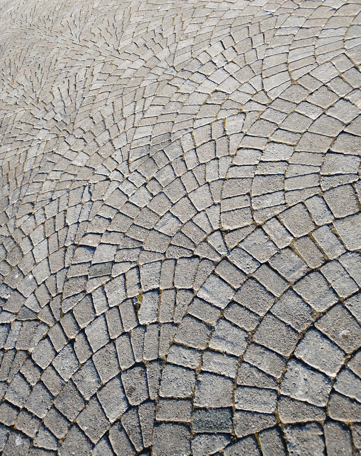 Overlapping circular shapes made of grey stone pavers that are appear to be quadrilateral or rectangular.