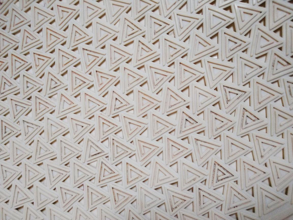 A near-monochrome image of many small connected triangles with triangular gaps between them. Each triangle has a spiral line in relief and they look like impossible triangles.