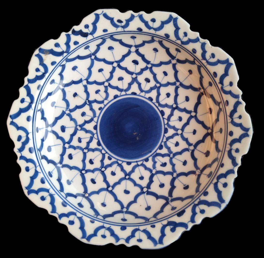 A blue and white dish photograph from above. It is a roundish octagon with scalloped edges. The patter has a central blue disc surrounded petals reminiscent of a sunflower or pineapple. The 12-pointed rosettes of different sizes appear to overlap.